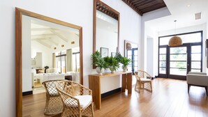 A spacious living room with a wooden floor, large mirrors, wicker chairs, and a console table with plants. - Villa Belvedere Pacific Sunsets 2 Private Pools (Nacascolo)