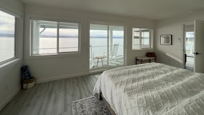 Un dormitorio con una cama grande, vista al agua y una silla junto a la ventana.