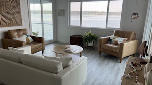 Una sala de estar moderna con dos sofás de cuero, una mesa de centro y vistas a una masa de agua a través de amplios ventanales.