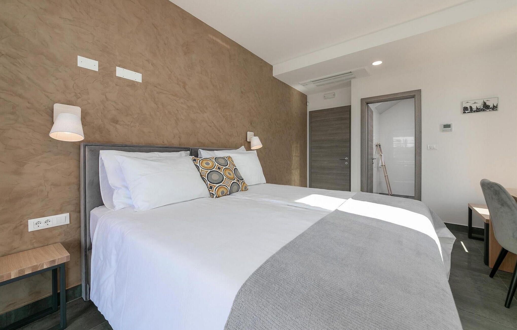 Ein modernes Hotelzimmer mit einem großen Bett, einem Nachttisch, einem Sessel und einer Tür zu einem Badezimmer.