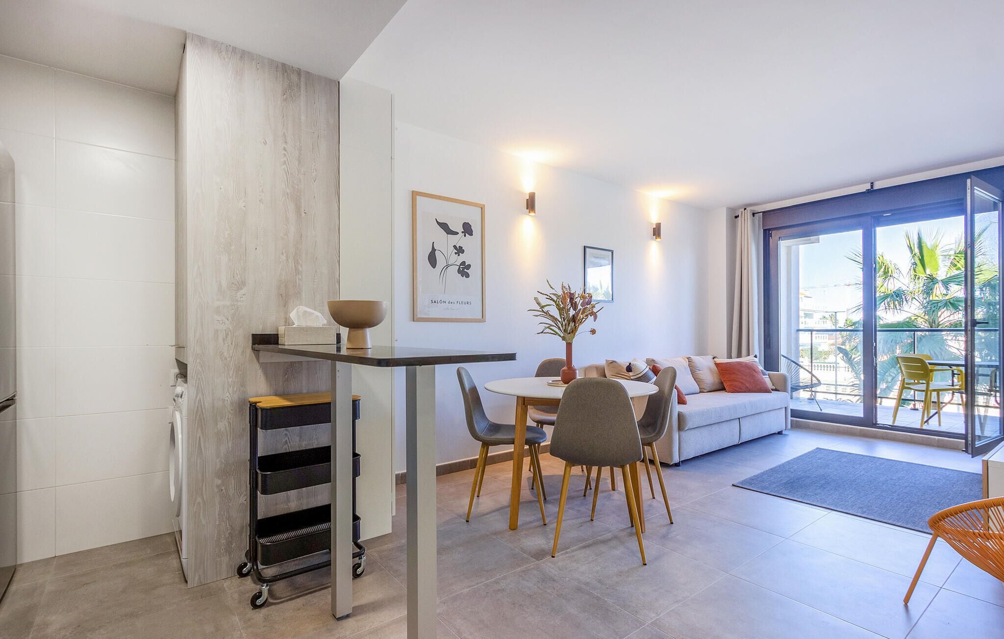 Un salon moderne comprenant un coin repas, un canapé et un balcon offrant une vue sur les palmiers.