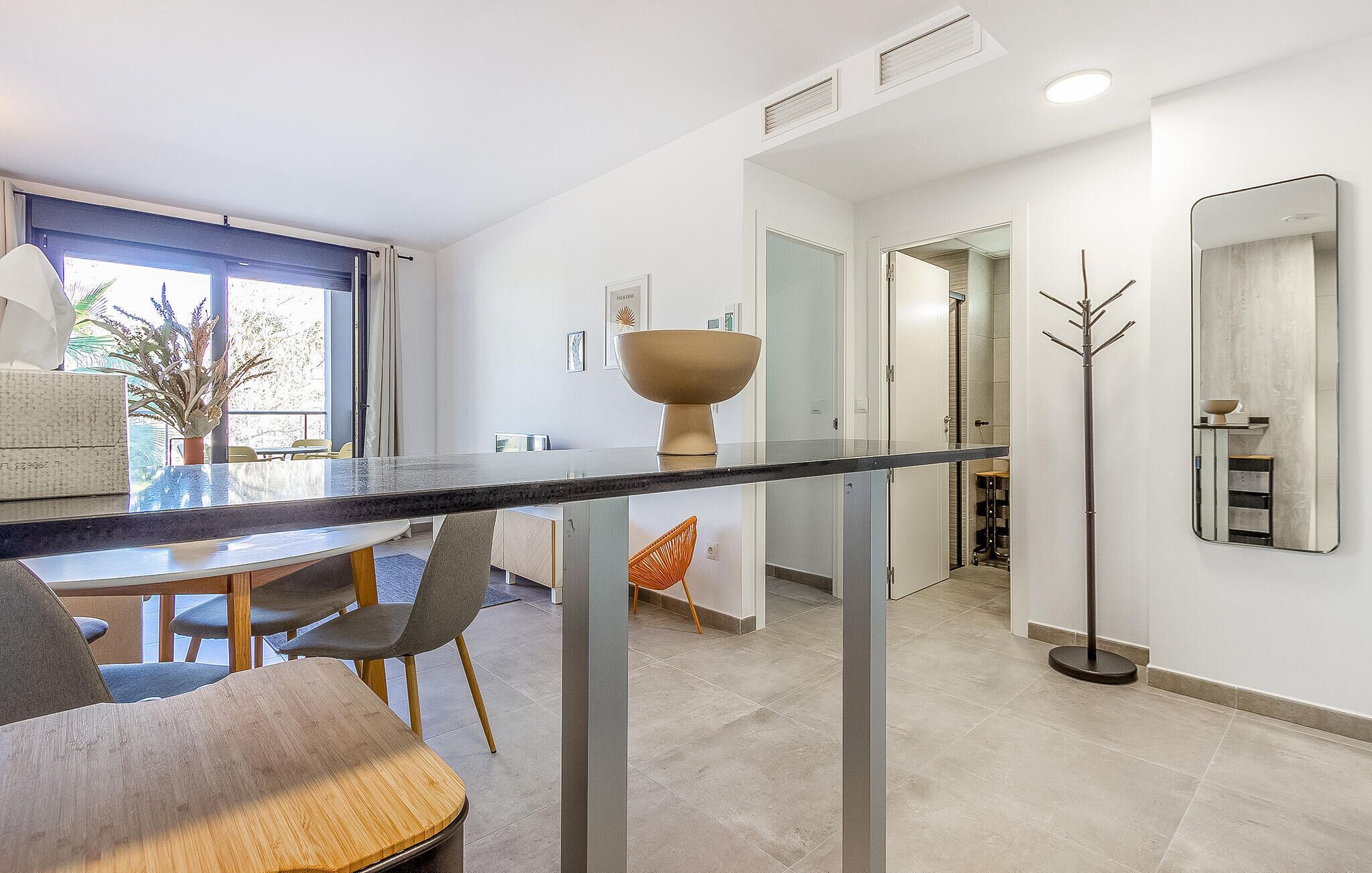 Un espace repas moderne avec une table à plateau en verre, des chaises grises et une table à manger en bois.