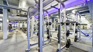 Ein modernes Fitnessstudio mit verschiedenen Gewichtstrainingsgeräten, darunter Squat-Stangen und Bänke.