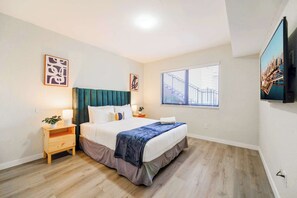 Un dormitorio con cama, mesitas de noche, ventana con persianas y obras de arte en las paredes.