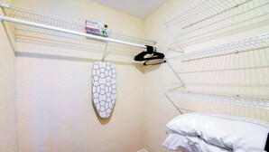 Een kleine, netjes ingerichte kamer met een stapelbed, een kledingrek en een wandgemonteerd strijkplank.