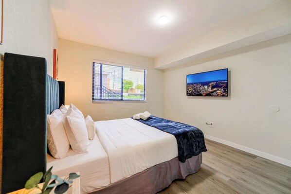 A hotel room with a bed, a window with blinds, a cityscape painting, and a ceiling light. - Apt w/ Free Parking | Stay in Little Havana (Miami)