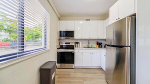 A compact kitchen with white cabinets, a stainless steel refrigerator, a microwave, an oven, and a dishwasher.