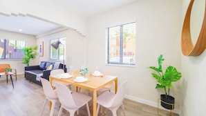 A modern living room with a dining table set for four, a sofa, and a large mirror on the wall.