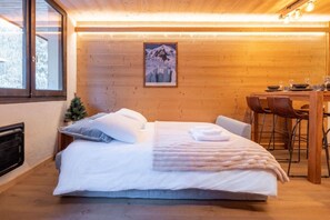 A cozy room with a bed, a dining table with chairs, a framed picture on the wall, and a window.