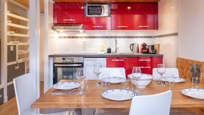 Cocina compacta con armarios rojos, microondas y comedor para cuatro personas con sillas y platos blancos.