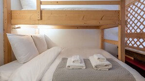 Una cama litera con ropa de cama y toallas blancas, un cabecero de madera y una ventana con celosía.