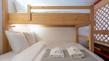 A bunk bed with white bedding and towels, a wooden headboard, and a lattice window.