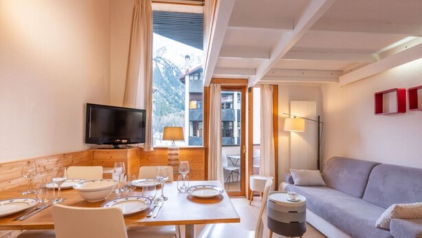 Comedor con mesa para cuatro, televisión y sofá en una habitación con vistas a montañas.