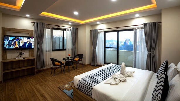 A hotel room with a large bed, a TV, a desk with two chairs, and a view of the city through the windows. - Hotel Travel Inn (Kathmandu)