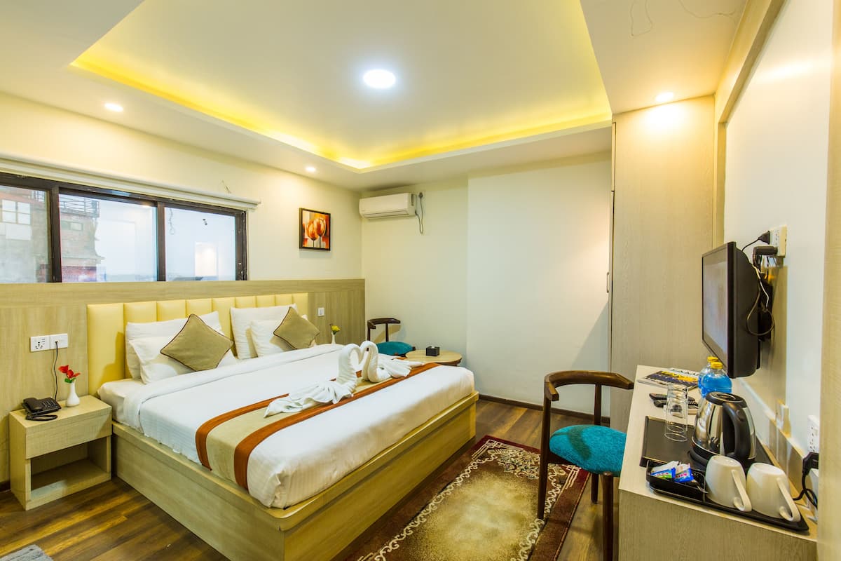 A hotel room with a bed, bedside table, chair, desk with a TV, and a window.