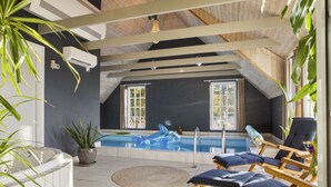 Ein modernes Hallenbad mit schrägverlaufender Decke, Liegestühlen und Topfpflanzen.