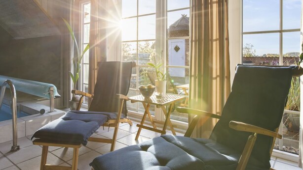 Ein sonnendurchflutetes Zimmer mit Pool, zwei Liegestühlen, einem Tisch und Blick ins Freie.