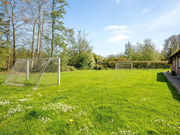 A well-maintained grassy field with two soccer goals, surrounded by trees and a building.