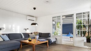 Ein modernes Wohnzimmer mit einem grauen Sofa, einem Holztisch und einer großen Glasschiebetür, die zu einem Außenbereich führt.