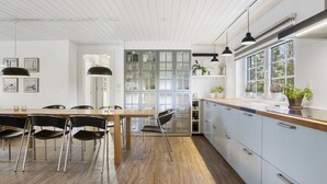 Eine moderne Küche mit Holzboden, einem Essbereich mit schwarzen Stühlen und einem Fenster mit Pflanzen.