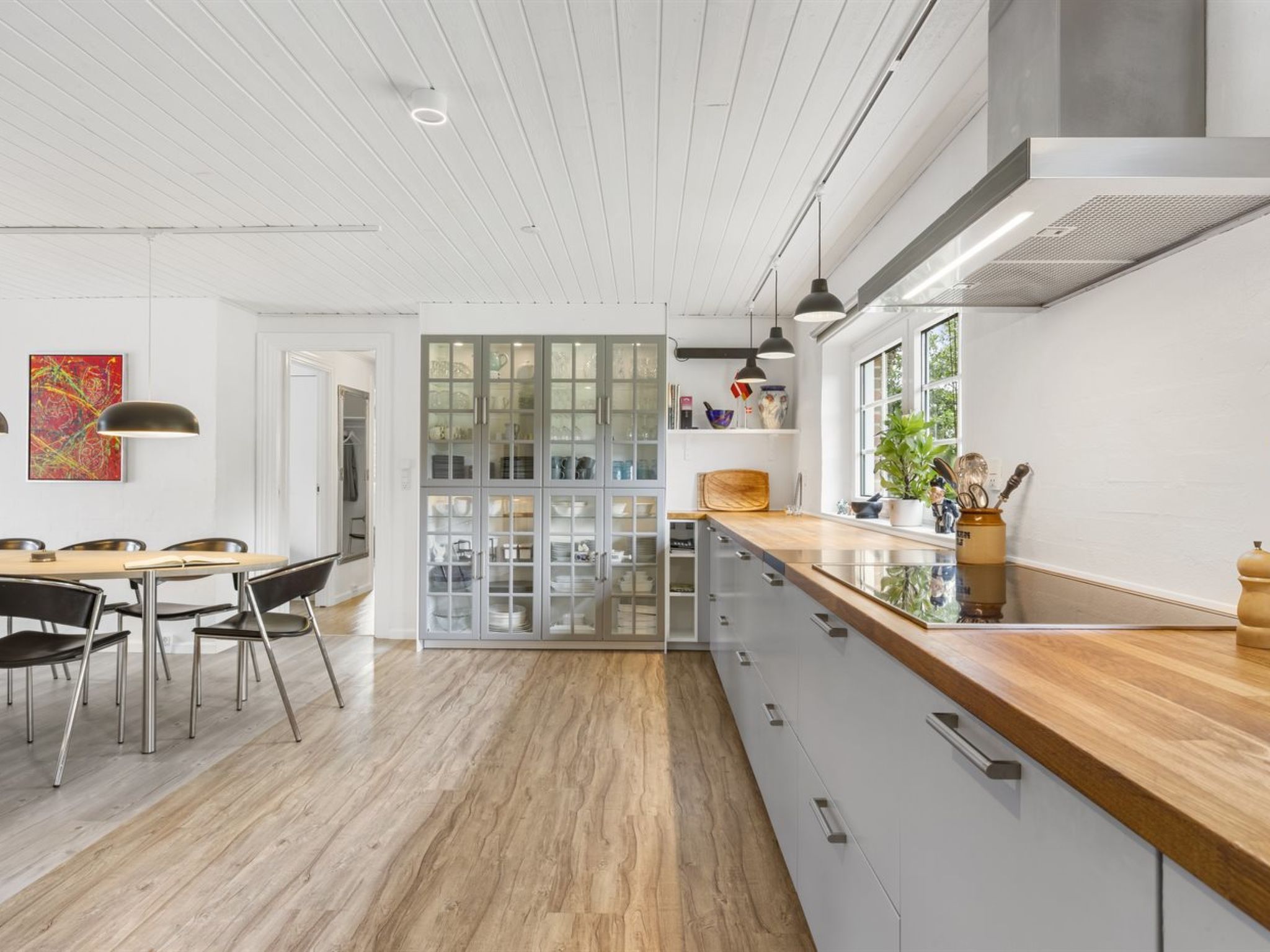 A modern kitchen with a wooden countertop, a dining area with chairs, and a large cabinet with glass doors.