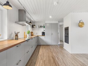 A modern kitchen with white cabinetry, wooden countertops, and pendant lighting.