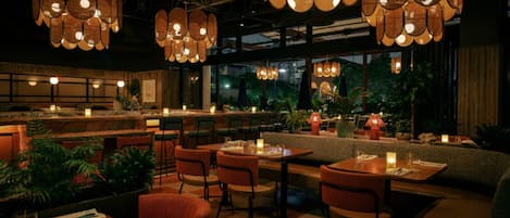 An indoor dining area with multiple tables and chairs, ambient lighting, and a view of the outdoors.