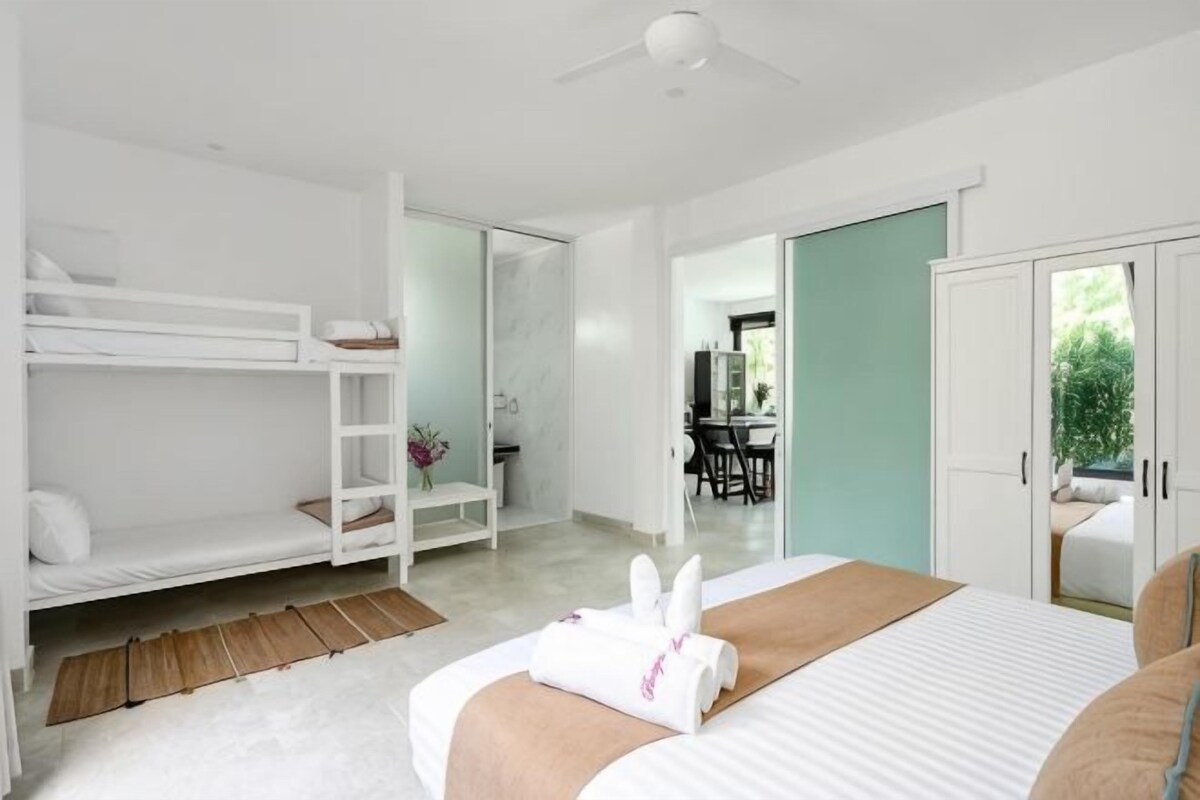 Een slaapkamer met een stapelbed, een enkel bed, een bureau en een badkamer.
