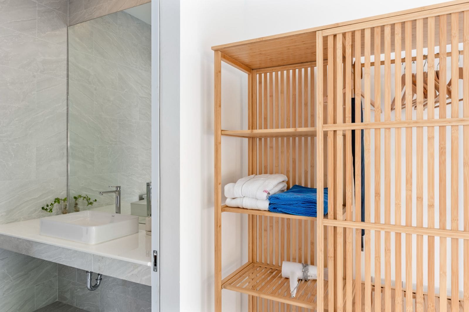 A bathroom with a white sink, mirror, and a wooden shelf unit with towels and a hairdryer.