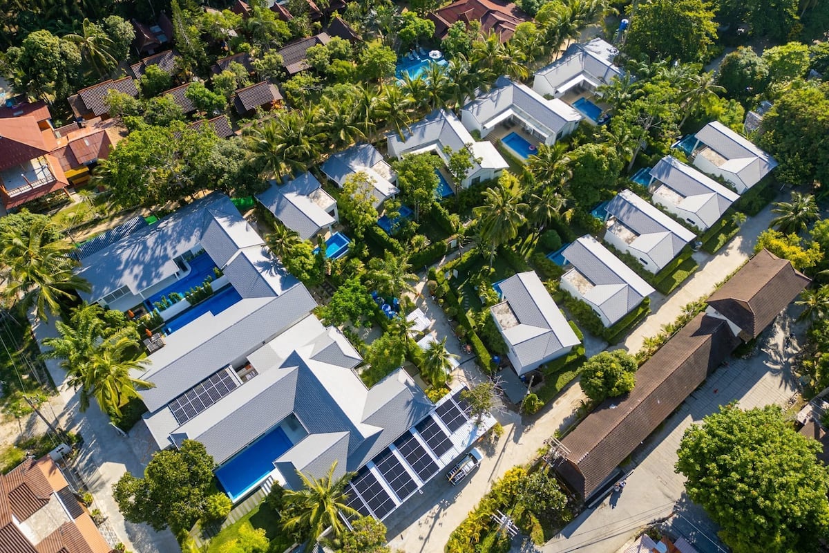 Vista aérea de una zona residencial con casas modernas, piscinas y abundante vegetación.