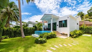 Une maison moderne avec une piscine, entourée de pelouses bien entretenues et de palmiers.