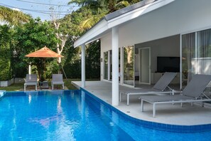 Ein moderner Poolbereich mit klarem, blauem Pool, Liegestühlen und einer überdachten Terrasse.