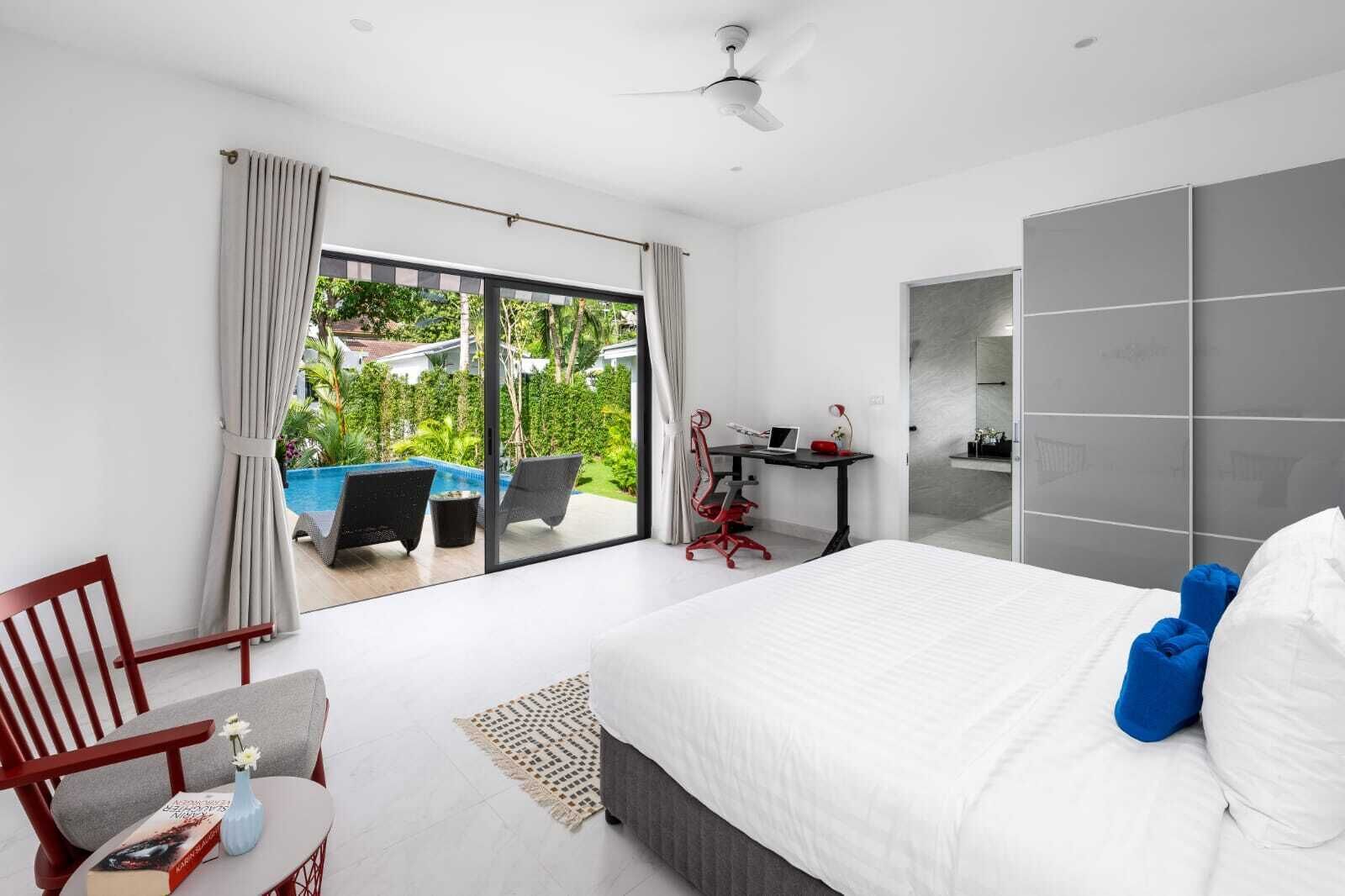 A modern bedroom with a large bed, a desk, and a view of a swimming pool.