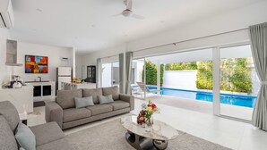 Un salon moderne avec un canapé gris, une table basse ornée de fleurs et une vue sur une piscine.