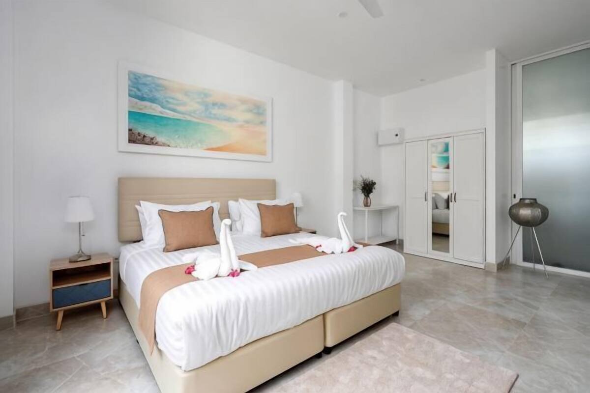 Habitación de hotel moderna con una cama grande, una mesita de noche, una lámpara, un cuadro y una puerta corredera al baño.
