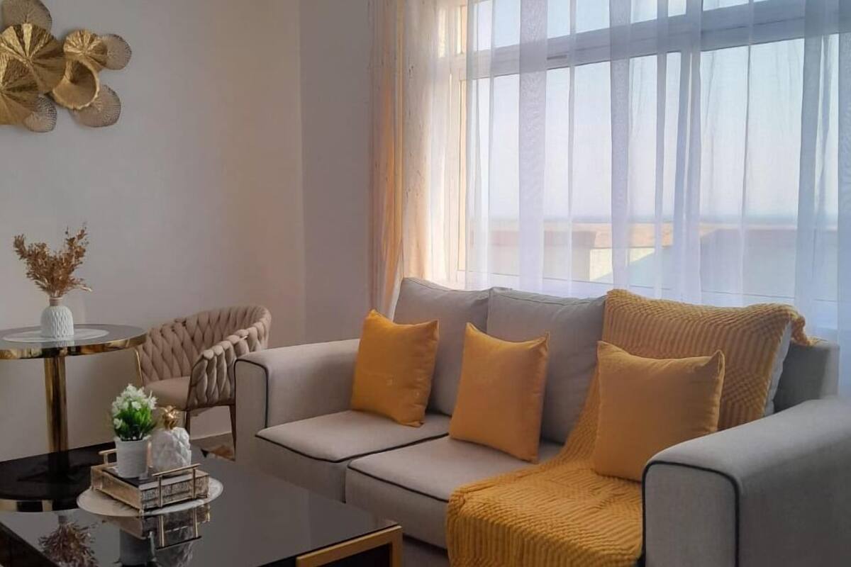 A modern living room with a grey sofa, yellow cushions, a black coffee table, and a chandelier.
