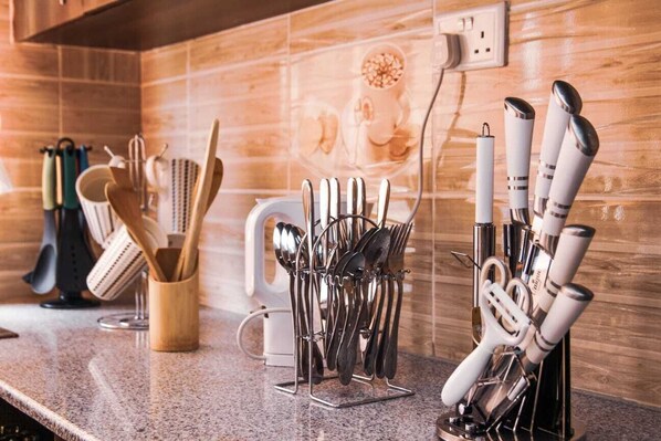 A kitchen counter with various utensils and cookware, including knives, spoons, and a grater.