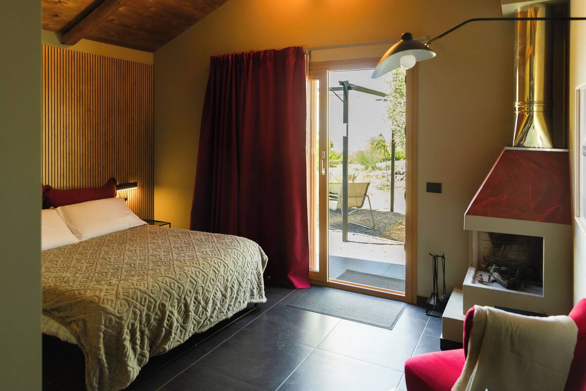 Une chambre à coucher avec un lit, un fauteuil rouge, une cheminée et une porte donnant sur l’extérieur.