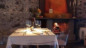 A dining table set with wine glasses, cutlery, and a candle holder, with a fireplace in the background.