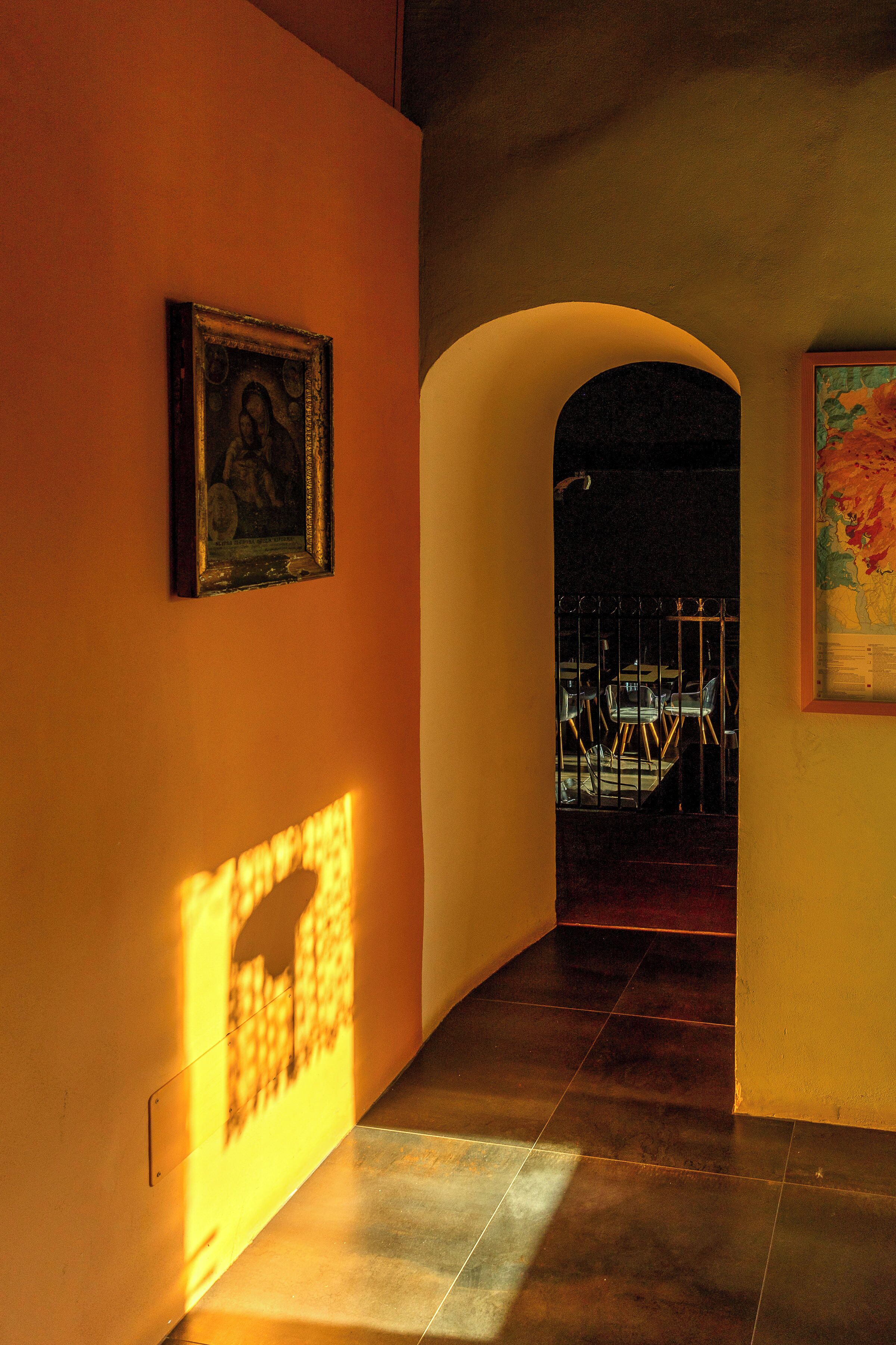 A hallway with a tiled floor, a framed picture on the wall, and an arched doorway leading to another room.