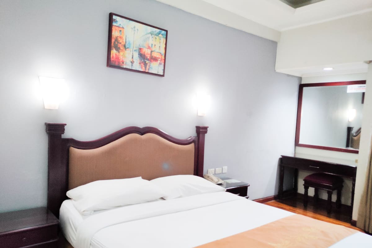 A hotel room with a bed, bedside table, and a mirror.