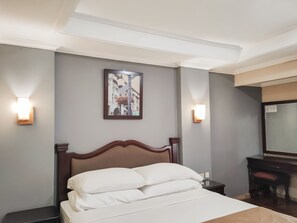 A hotel room with a bed, two wall-mounted light fixtures, a framed picture, and a desk with a chair. - Hotel Menteng 2 (Jakarta)
