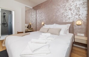 Ein modernes Hotelzimmer mit einem großen Bett, einer Duschkabine aus Glas und einer Wand mit Marmorstruktur.