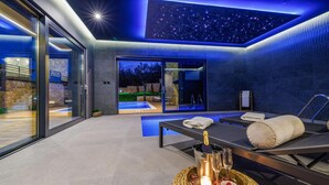 A modern spa room with a glass wall, a massage table, and a small pool.