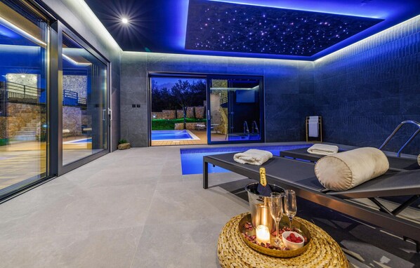 Ein moderner Spa-Raum mit Glaswand, einer Massageliege und einem kleinen Pool.