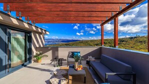 A modern outdoor balcony with a view of a mountainous landscape, furnished with a sofa, table, and chairs.