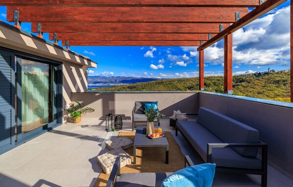 Ein moderner Balkon mit Blick auf eine gebirgige Landschaft, ausgestattet mit einer Couch, einem Tisch und Stühlen.