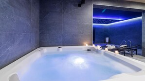 A modern spa room with a large hot tub, a massage table, and a wall with a starry sky design.