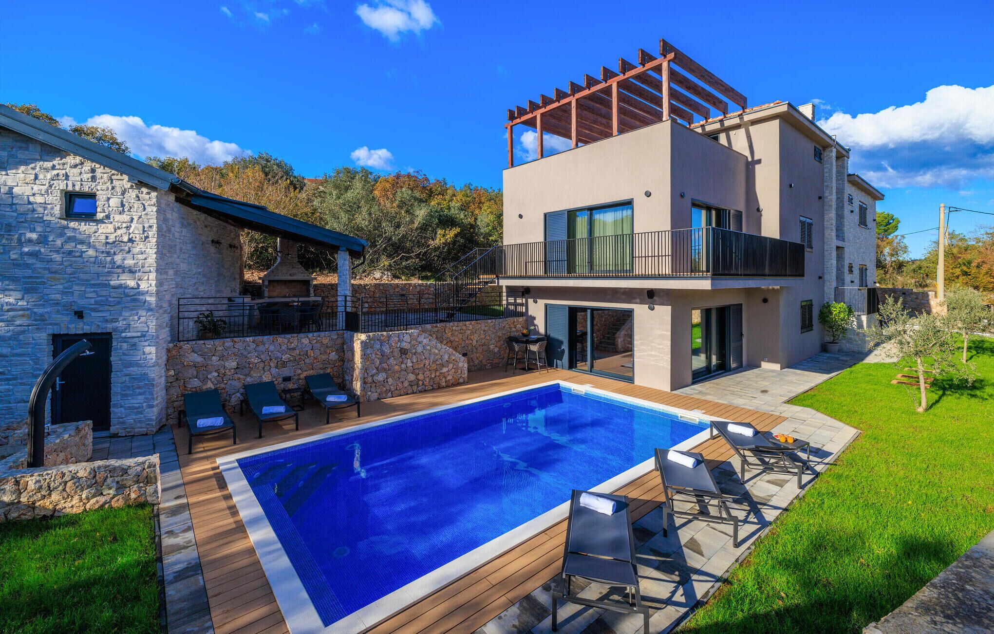 A modern two-story house with a swimming pool, outdoor seating, and a stone wall.