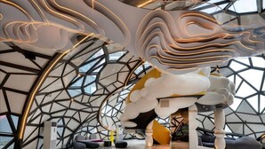 Un interior moderno con diseño geométrico en el techo, un elemento escultórico central y una cúpula de cristal.